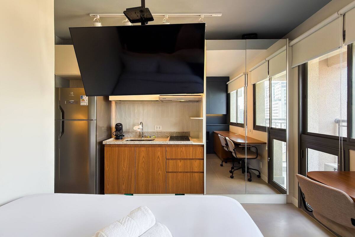 Ein modernes Hotelzimmer mit einem großen Bett, einer Holzküchenzeile, einem Essbereich und Blick durch große Fenster.