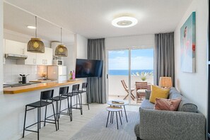 A modern kitchen with a flat-screen TV, a dining area with bar stools, a sofa, and a balcony with a view. - Vacation Apartment 'Playa La Arena 2 Bed' with Sea View, Balcony and Wi-Fi (Puerto de Santiago)