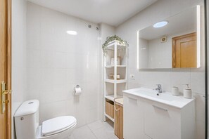 A modern bathroom with a toilet, sink, mirror, and shelves.