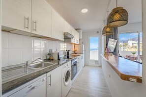 A modern kitchen with white cabinets, a built-in washing machine, and a view of the city through large windows.