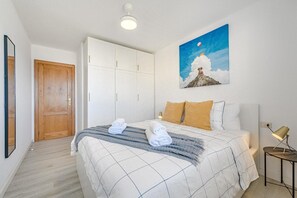 A bedroom with a bed, a wooden door, a wardrobe, a painting, and a bedside lamp.