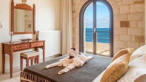 A bedroom with a bed, a wooden dresser, a mirror, and a view of the sea through a glass door. - Xristinas Apartments - Aphrodite Sea View (Kolymvari)
