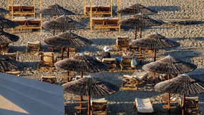 A beach with wooden lounge chairs and thatched umbrellas, a rocky breakwater, and calm sea. - Xristinas Apartments - Artemis (Kolymvari)