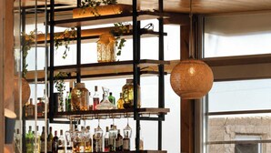 A bar area with shelves of bottles, a hanging basket, stools, and a counter with coffee machines. - Xristinas Apartments - Artemis (Kolymvari)