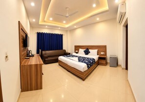 A hotel room with a bed, a sofa, a desk, and a TV.
