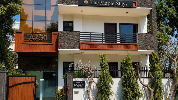 Ein mehrstöckiges Hotel mit modernem Design, das mit Balkonen und einem gut sichtbaren Schild für 'The Maple Stays' versehen ist.