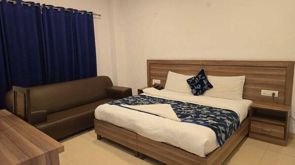 Une chambre à coucher avec un lit, une tête de lit en bois, une table de chevet, une commode, un canapé marron et un rideau bleu.