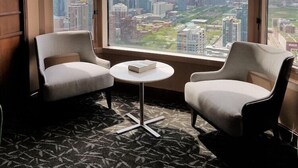 A room with two chairs, a small table, and a large window offering a city view. - The Buckingham Athletic Club & Hotel (Chicago)