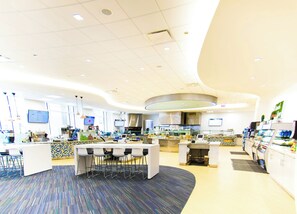 A modern restaurant interior with a central bar area, multiple seating options, and a kitchen in the background. - The Buckingham Athletic Club & Hotel (Chicago)