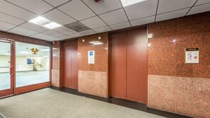 A hallway with elevators, a glass door entrance, and a bulletin board with notices. - The Buckingham Athletic Club & Hotel (Chicago)