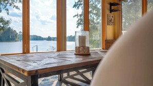 Une table en bois surmontée d’un chandelier en verre, dans une pièce dotée de grandes fenêtres donnant sur un lac.
