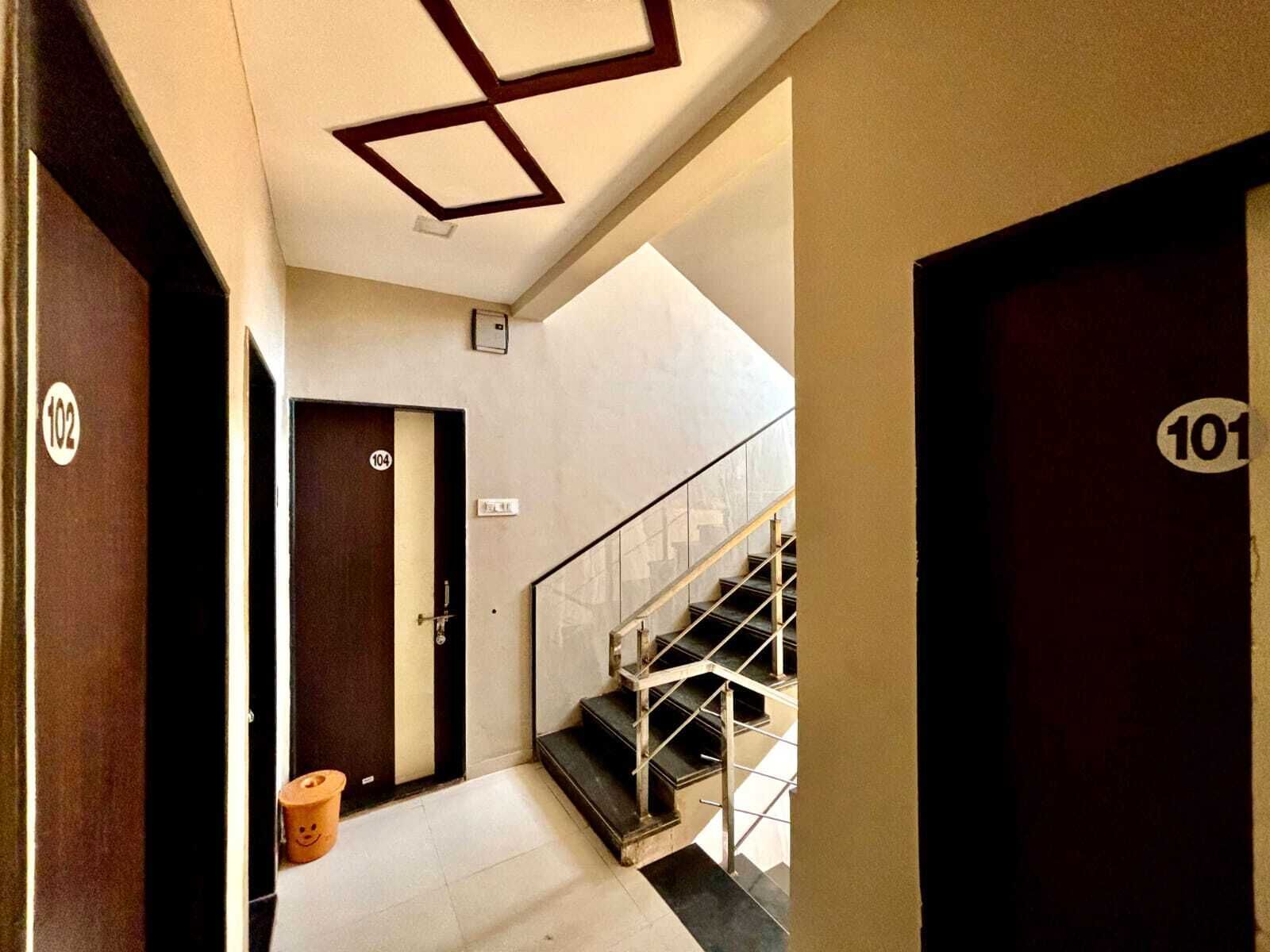 Un pasillo con una escalera, una puerta con el número 104 y un cubo de basura con una carita sonriente.