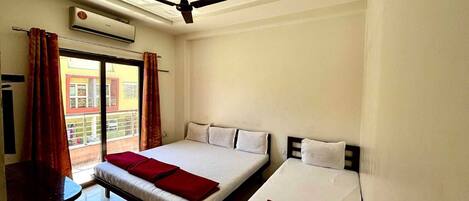 Habitación de hotel con dos camas, ventilador de techo, aire acondicionado y vista al balcón exterior.