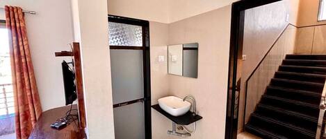 A modern bathroom with a white sink, a mirror, and a black staircase.