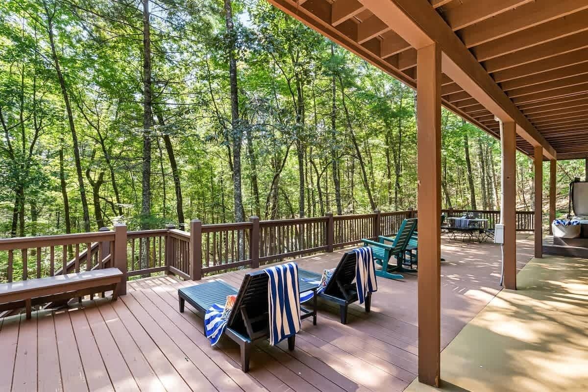 A covered deck with wooden railings, lounge chairs with striped towels, and a view of a dense forest.