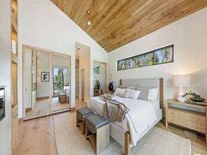 A bedroom with a large bed, wooden ceiling, and a view of the outdoors.