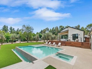 A modern house with a swimming pool, outdoor seating, and a well-maintained lawn.