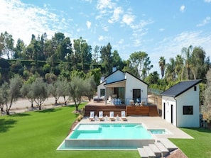Uma casa moderna com piscina, um deck com espreguiçadeiras e um grande jardim.