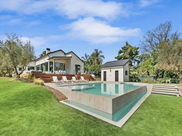 A modern house with a swimming pool, a covered patio, and a well-maintained lawn.