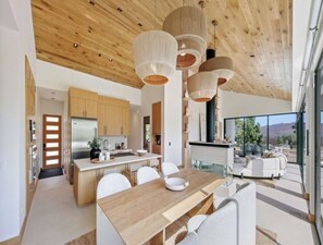 A modern kitchen with wooden cabinets, a stainless steel refrigerator, and a dining area with a wooden table and white chairs.