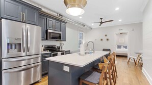 A modern kitchen with stainless steel appliances, a central island with bar stools, and a ceiling fan. - Stylish, Downtown Charleston 2bd Home w. Porch! (Charleston)