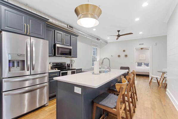 A modern kitchen with stainless steel appliances, a central island with bar stools, and a ceiling fan.