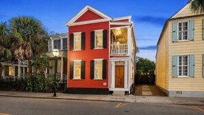 A two-story building with a red facade, a balcony, and a wooden door marked '81'. - Stylish, Downtown Charleston 2bd Home w. Porch! (Charleston)