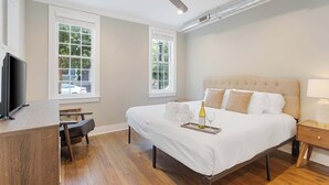 A bedroom with a bed, a desk, a chair, a television, and two windows. - Stylish, Downtown Charleston 2bd Home w. Porch! (Charleston)