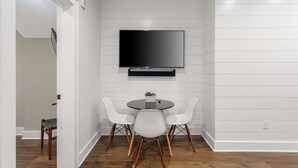 A modern dining area with a round table, two white chairs, and a flat-screen TV mounted on the wall. - Stylish, Downtown Charleston 2bd Home w. Porch! (Charleston)
