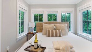 A bedroom with a large bed, multiple pillows, a bedside table with a lamp, and a tray with a bottle and glasses. - 2bd Home, Large Private Backyard + Blocks to King! (Charleston)