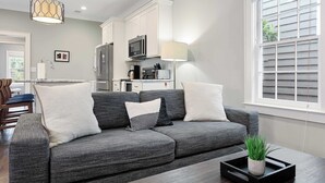 A modern living room with a grey sofa, a coffee table, and a dining area in the background.
