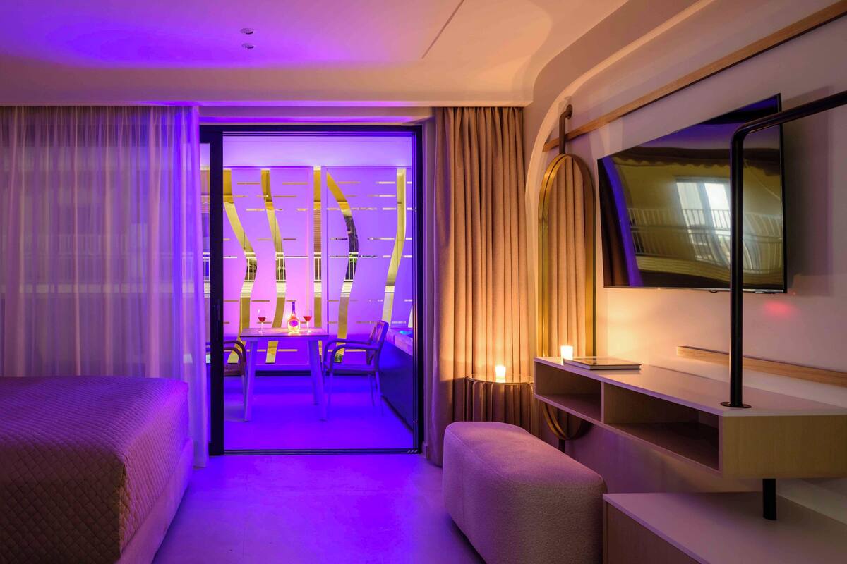 A hotel room with a bed, a seating area, a TV, and a view through a glass door.
