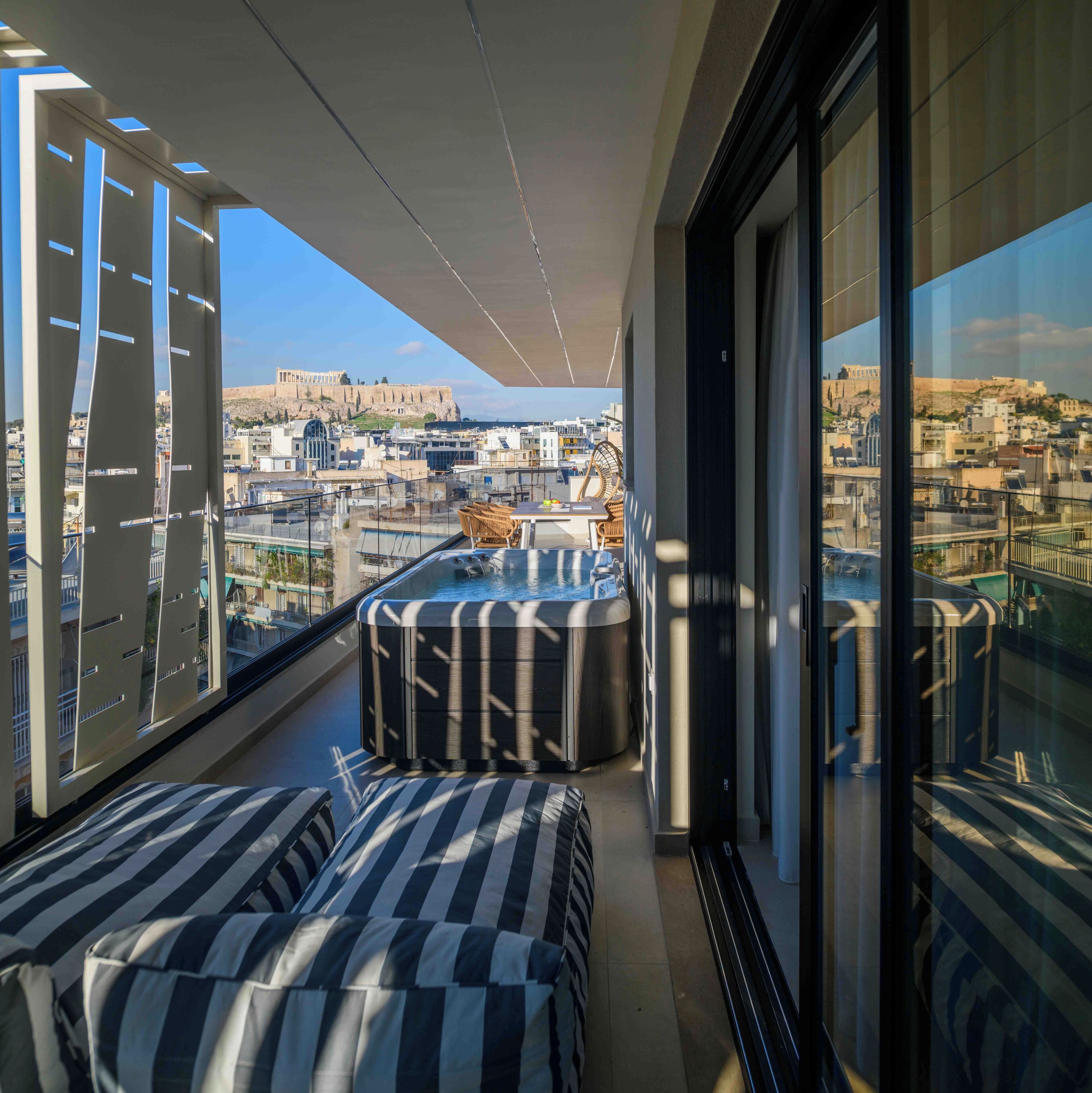 A balcony with a hot tub, striped cushions, and a view of a cityscape including a historic building.