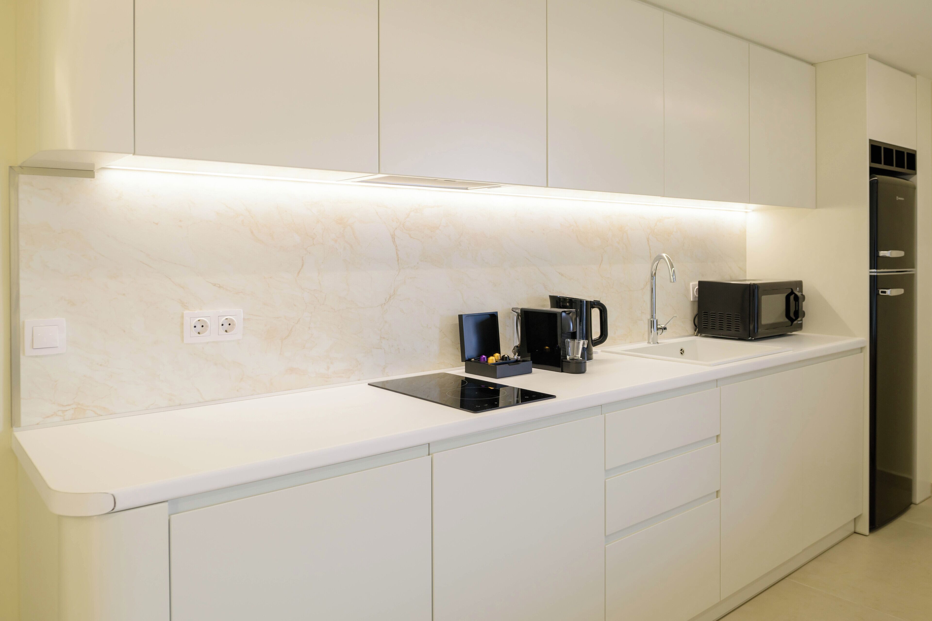 Eine moderne Küche mit weißen Schränken, einer schwarzen Kaffeemaschine, einer Mikrowelle und einem eingebauten Backofen.