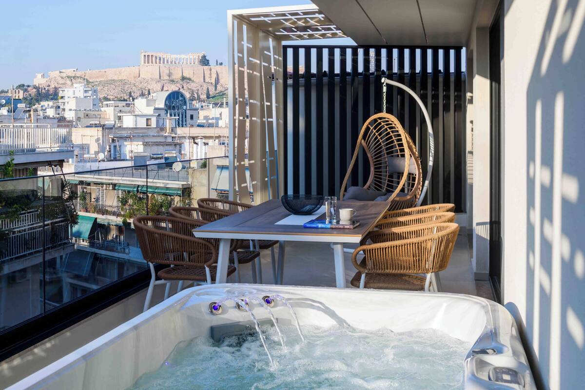 A balcony with a hot tub, wicker chairs, and a table.