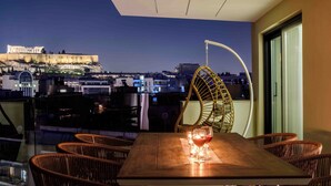 A balcony with wicker chairs and a table, overlooking a cityscape with a historic building in the background. - Thea Acropolis Suites & Apartments (Athens)