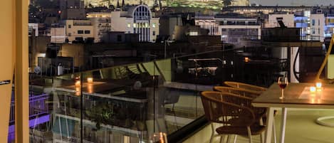 A rooftop terrace with a hot tub, a table with chairs, and a view of a historic building in the background.