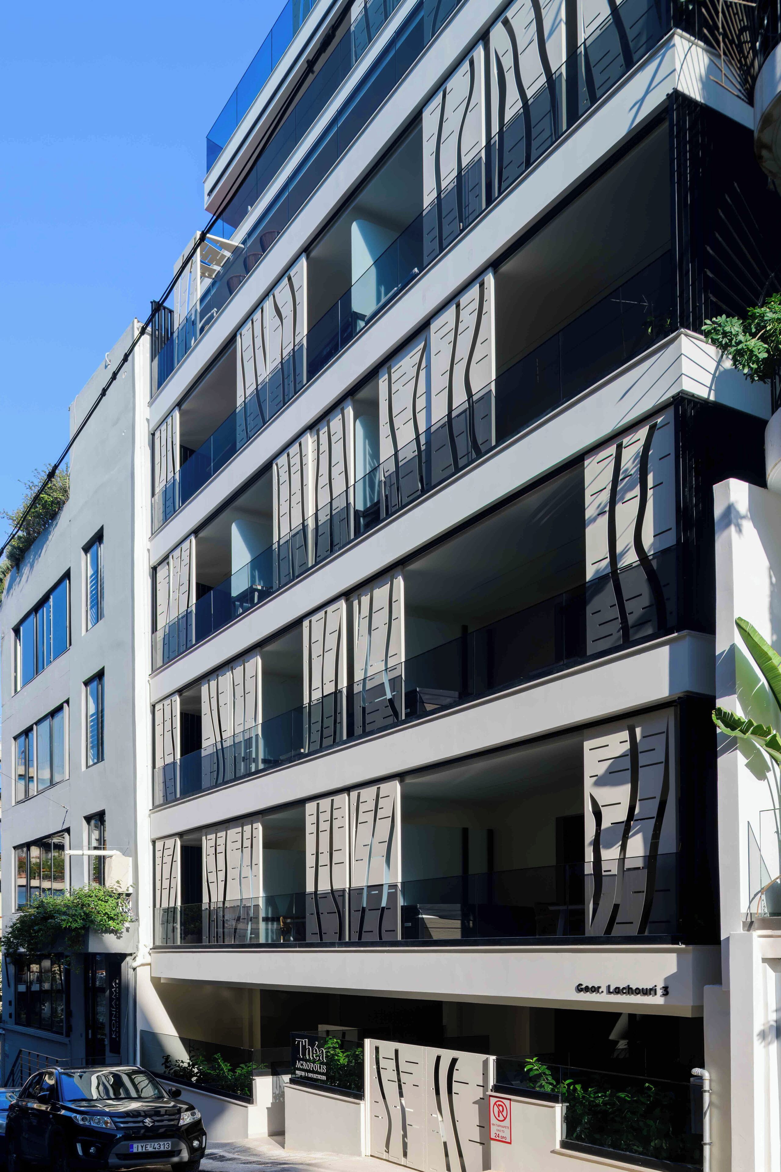 A modern multi-story building with balconies, large windows, and a sign indicating "Thea Acconci".