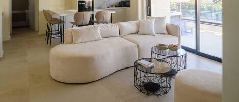 A modern living room with a sectional sofa, a dining area with chairs, and a kitchen in the background.