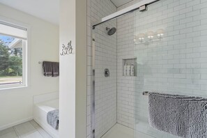 Ein modernes Badezimmer mit weißen Fliesen, einer Glasdusche, einer Badewanne und einem Handtuchhalter mit einem Handtuch.