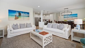 Een ruime woonkamer met twee witte banken, een salontafel en een eethoek met houten stoelen.