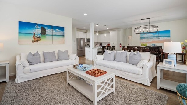 A spacious living room with two white sofas, a coffee table, and a dining area with wooden chairs. - Large Family Home on Golf Course. Short Walk to Beach. Private Workspace. (Seaside)