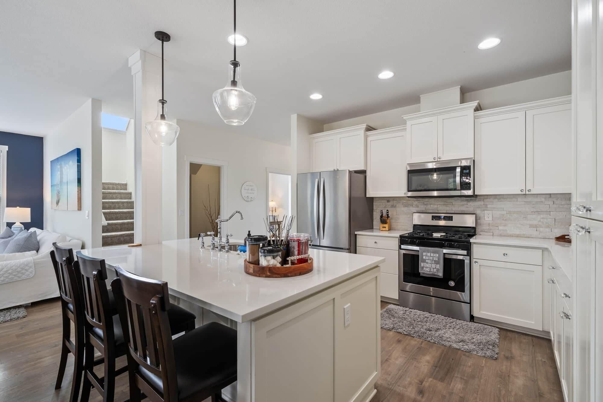 A modern kitchen with white cabinetry, stainless steel appliances, and a central island with bar stools.