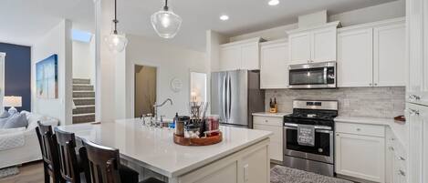 A modern kitchen with white cabinetry, stainless steel appliances, and a central island with bar stools.