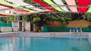 Μια πισίνα με πλακάκια περιμετρικά, που περιβάλλεται από μια σκεπαστή περιοχή με πολύχρωμα υφάσματα.
