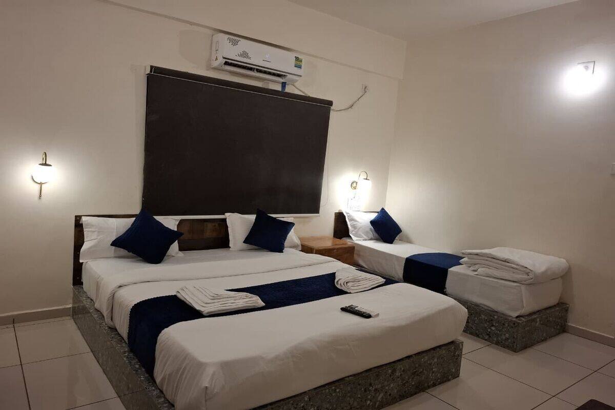 Habitació d'hotel amb dos llits, un capçal de llit gran i fosc, un aparell d'aire condicionat i llums penjades a la paret.