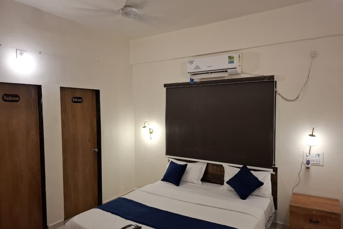 Une chambre d’hôtel comprenant un lit, une table de chevet, une armoire, un panneau indiquant la présence d’un balcon, un appareil de climatisation et un luminaire fixé au mur.