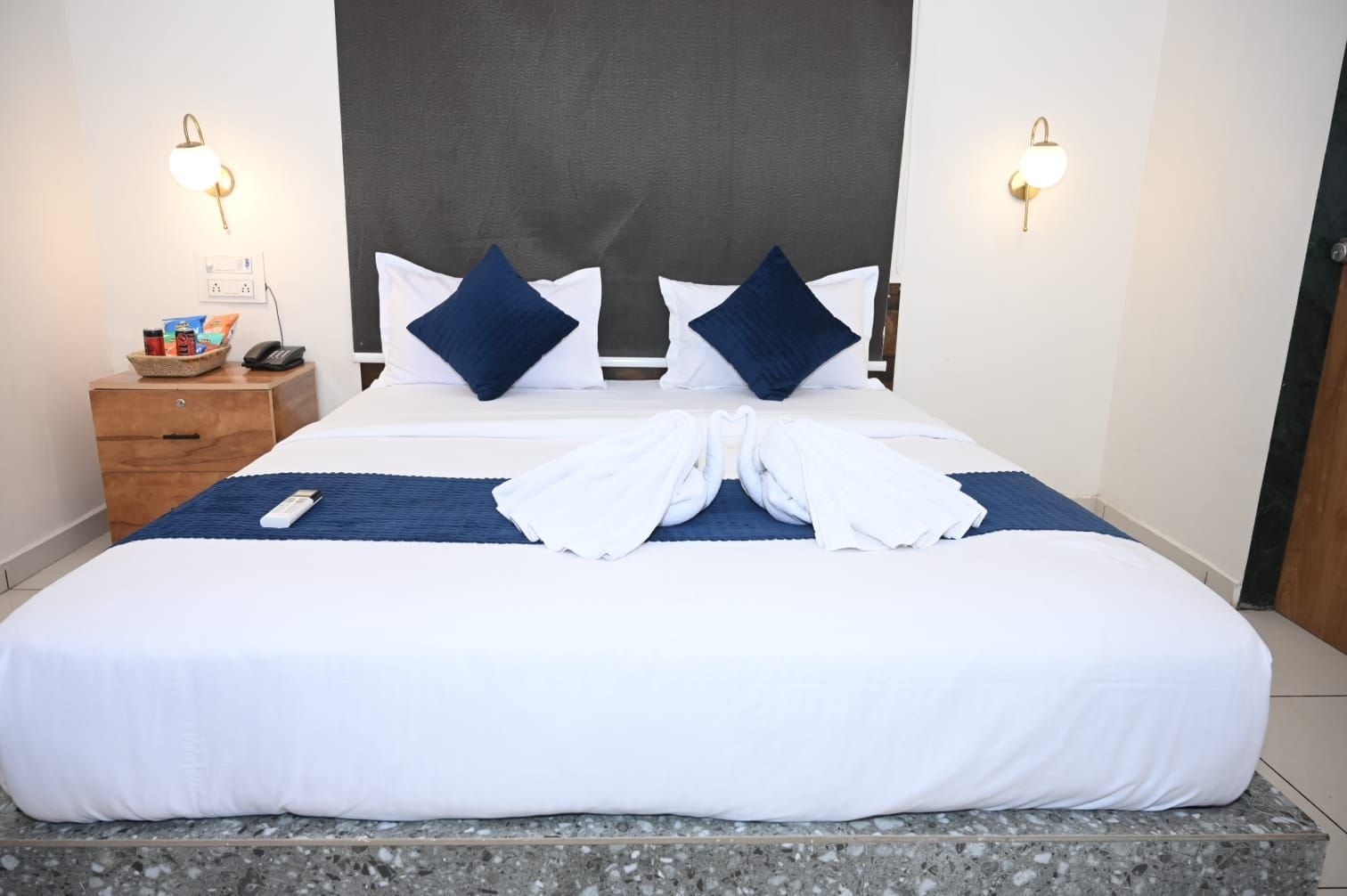 Cama bem arrumada com cabeceira, duas mesas de cabeceira e luminária fixada na parede.