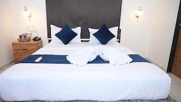 Cama bem arrumada com cabeceira, duas mesas de cabeceira e luminária fixada na parede.