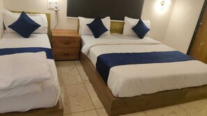 Hotellihuoneessa on kaksi erillistä sänkyä, joissa on molemmissa puinen pääty ja valkoiset vuodevaatteet sekä siniset yksityiskohdat. Sänkyjen välissä on puinen yöpöytä ja vasemman sängyn yläpuolella seinäpistorasia.